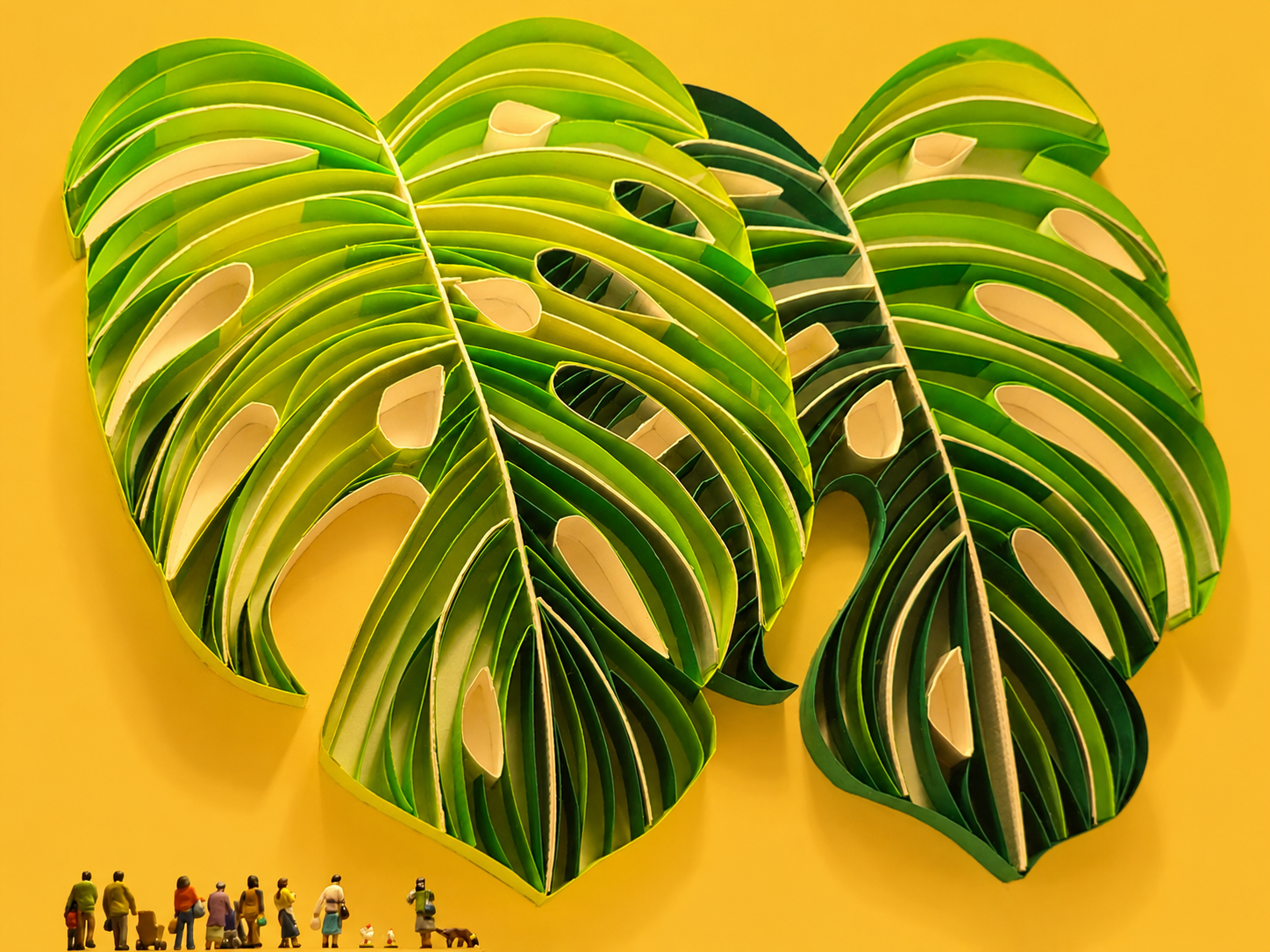 Layered green Monstera-leaf sculptures with miniature visitors against a warm golden wall