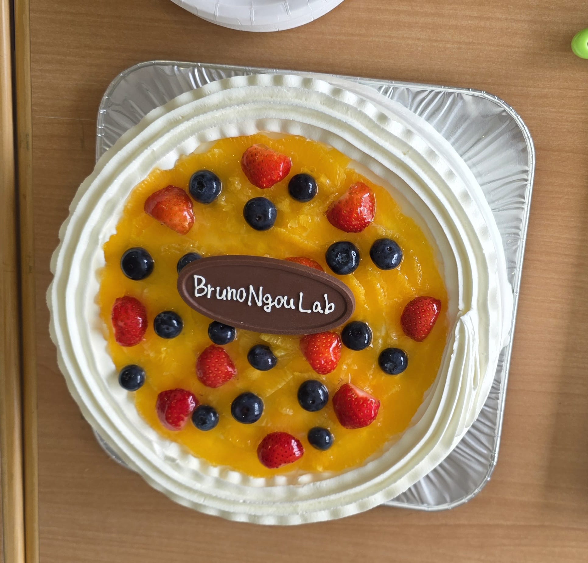 Fruit-topped opening-day cake with a Bruno Ngou Lab chocolate plaque