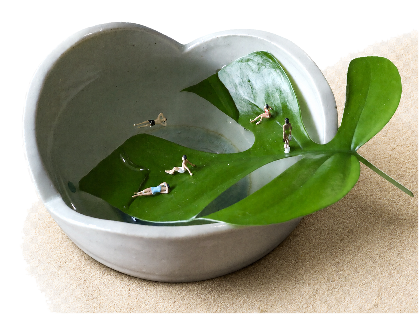 A heart-shaped ceramic bowl filled with water and leaves, with miniature people relaxing among the leaves.